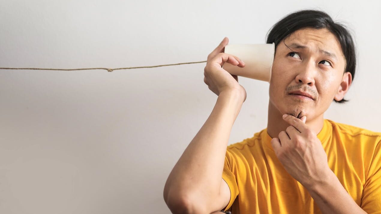 pensive ethnic man listening to answer in paper cup phone