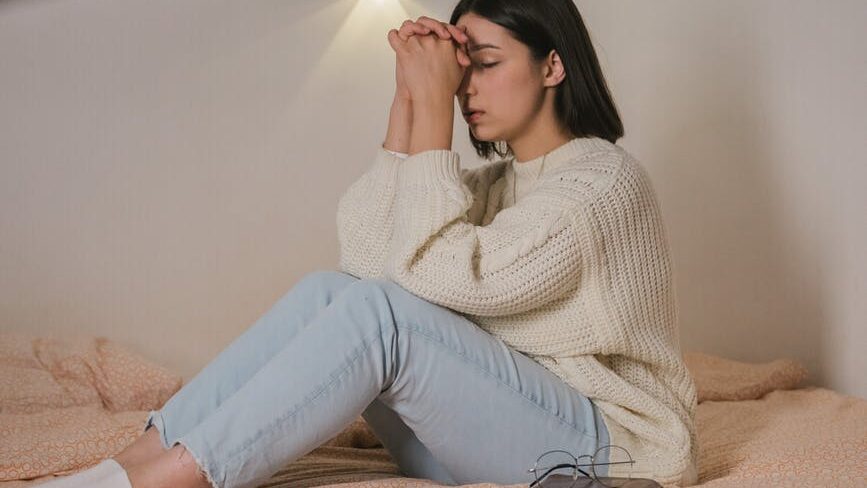 woman in white sweater and blue denim jeans sitting on bed